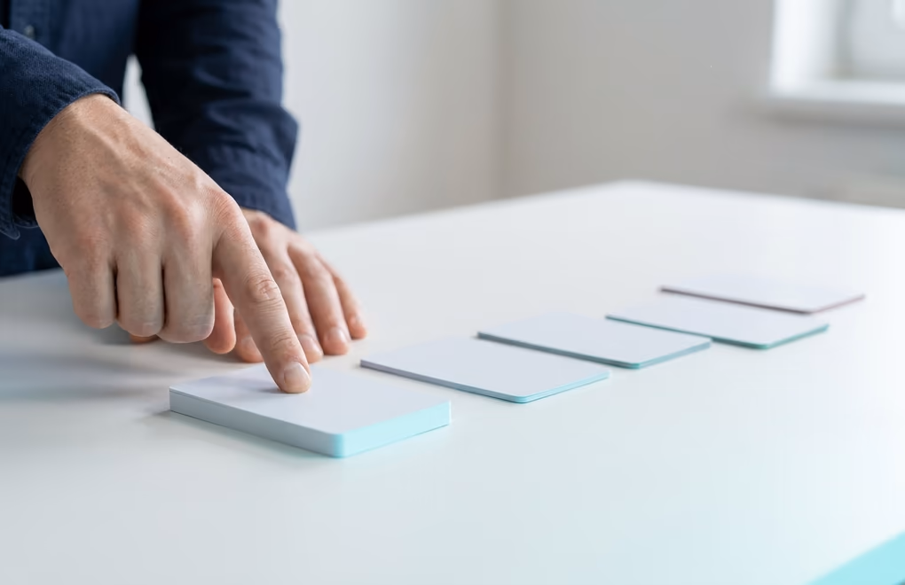 Hands arranging blank channel cards into a priority order on a bright table, one card placed first
