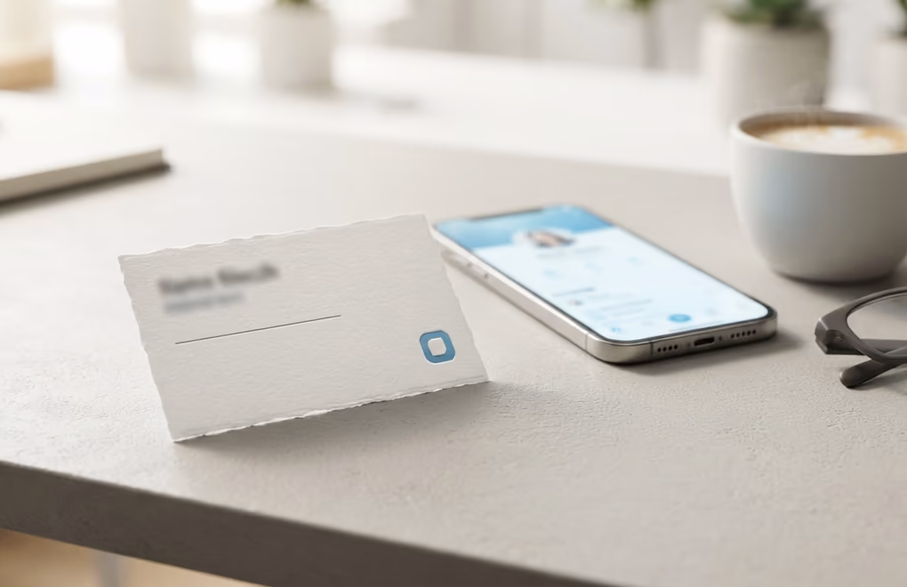 A business card and phone on a desk showing a personal profile link
